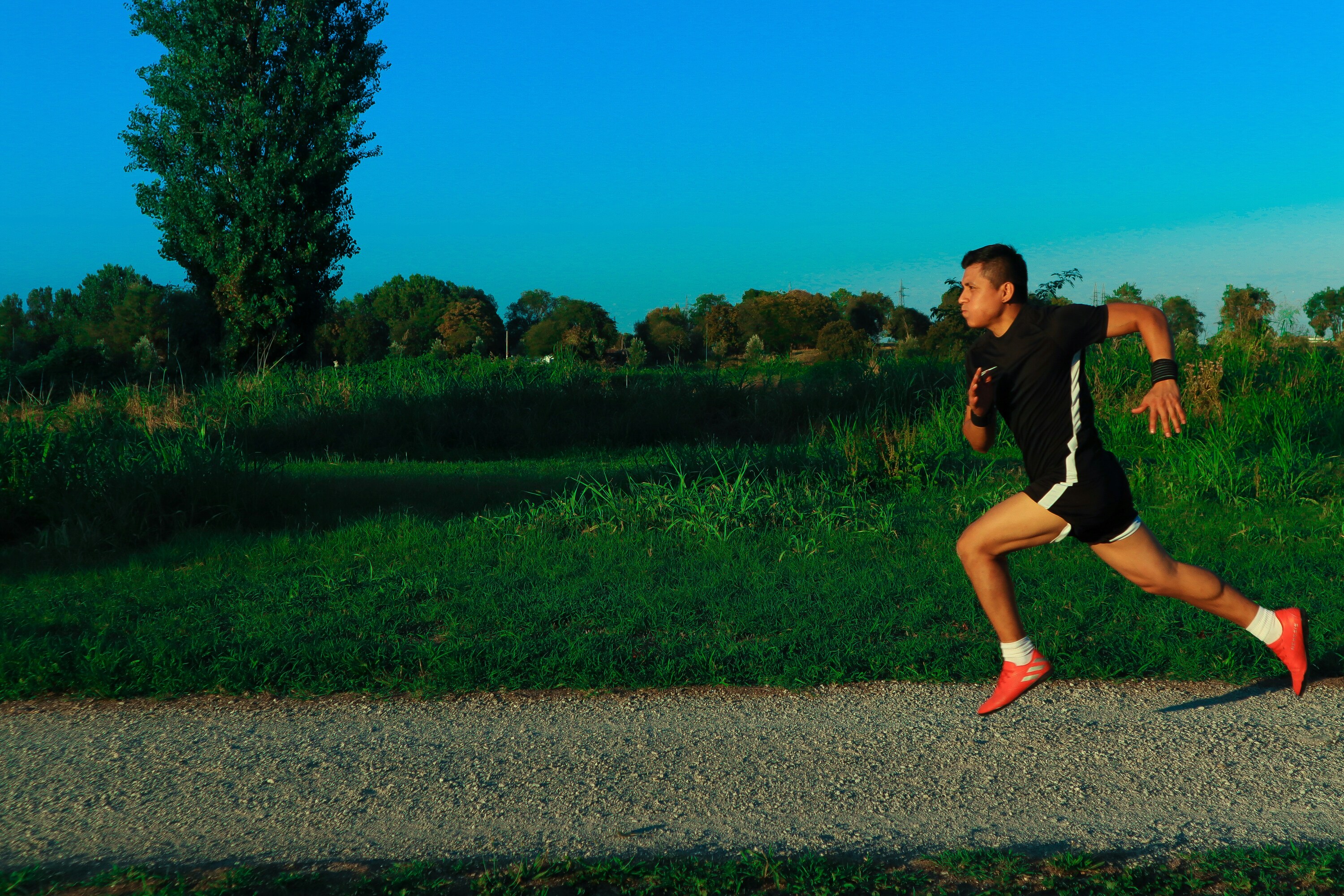 man running on a gravel path through a green meadow under a clear blue sky
