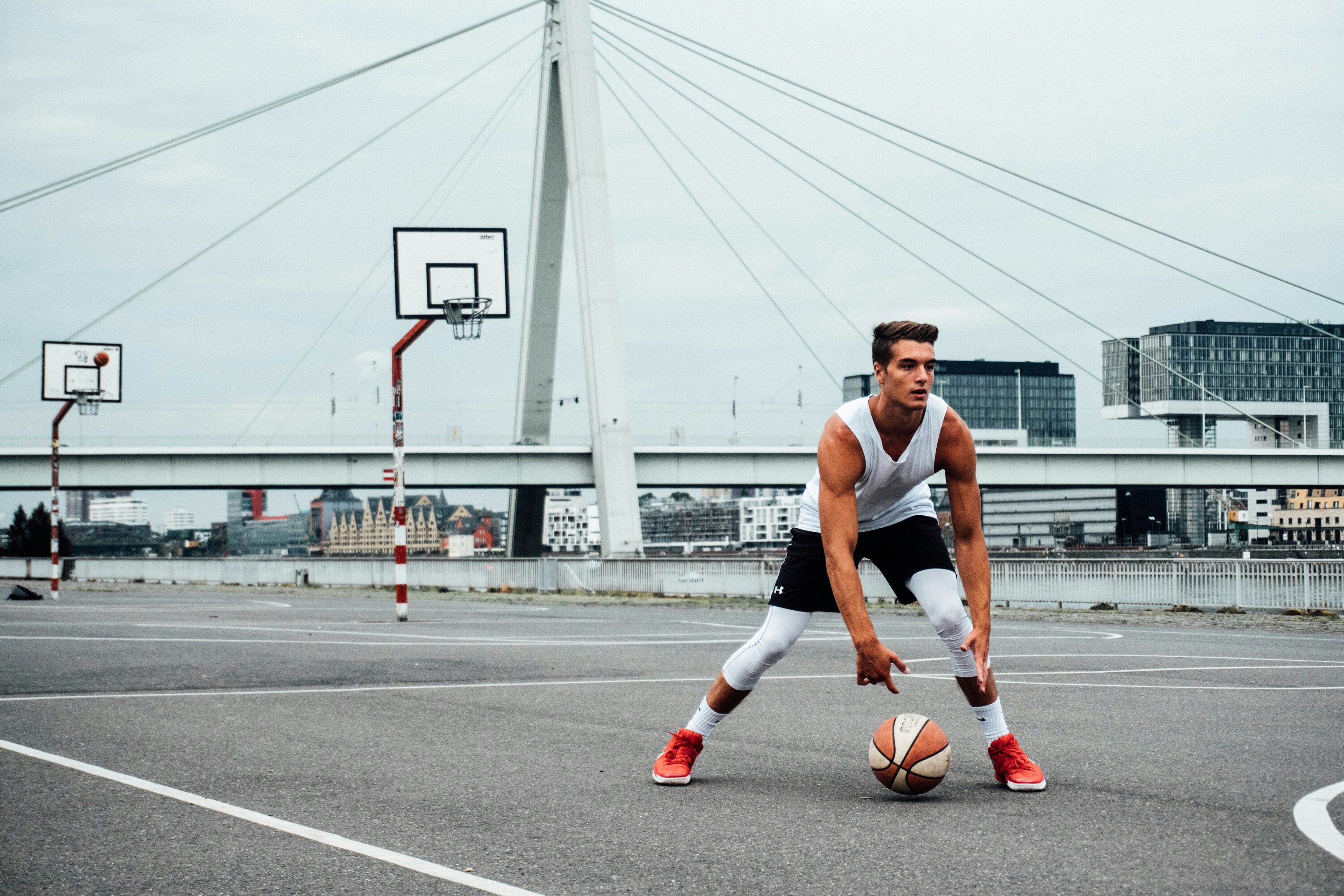 young man dribbling a basketball on an outdoor court near a cable-stayed bridge